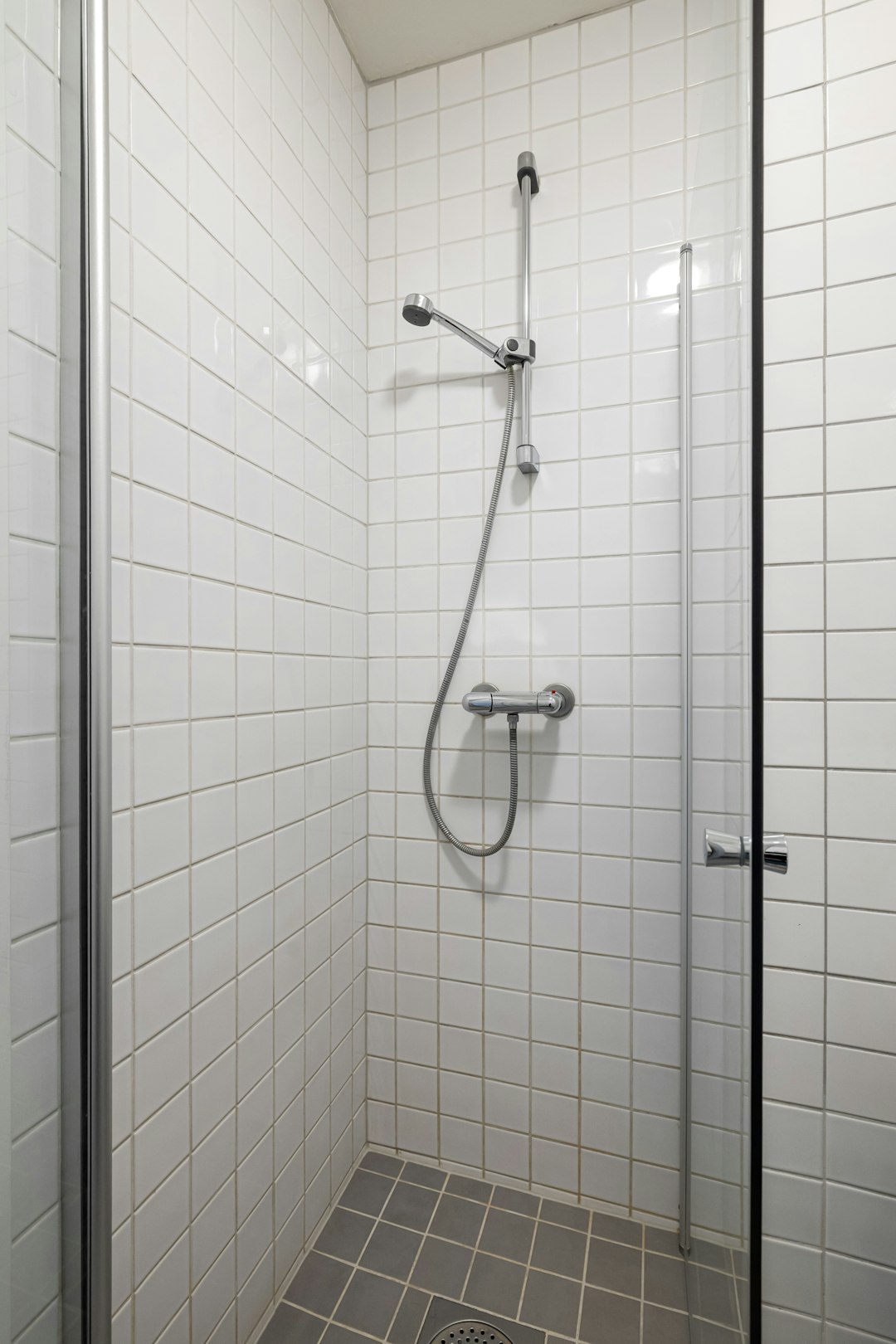 a-walk-in-shower-sitting-next-to-a-white-tiled-wall-hdpt79bwbgw